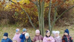 Grupa dzieci stoi przy jesiennym drzewie w parku