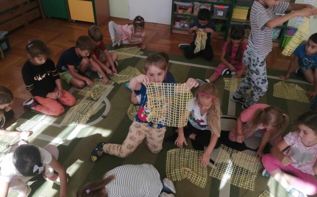 Dzieci przeplatają włóczkę przez materiał z dziurkami