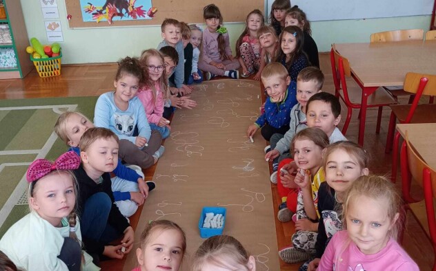 Dzieci siedzą wzdłuż długiego arkuszu papieru.
